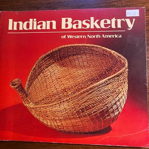 Puede incluir: Un libro titulado "Indian Basketry of Western North America" con una cesta tejida en la portada. La cesta es marrón y tiene una forma única con un pico.