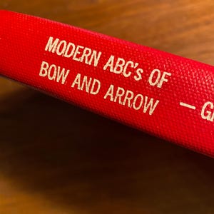 Può includere: Un libro rosso con il titolo "MODERN ABC's OF BOW AND ARROW - G"