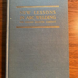 May include: A blue hardcover book with gold lettering that reads "New Lessons in Arc Welding" and "The Lincoln Electric Company".