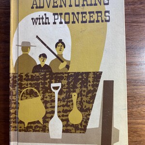 以下が含まれることがあります： 黄色い背景に茶色の文字で「Adventuring with Pioneers」というタイトルが書かれた、ビンテージな本の表紙。表紙には、ワゴンと3人の人物、鍋、シャベル、お玉が描かれた、スタイリッシュなイラストが描かれている。
