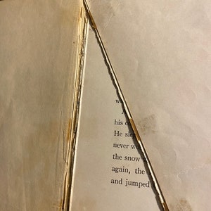 K&ouml;nnte beinhalten: Nahaufnahme eines Buches mit einer zerrissenen Seite. Der Text auf der Seite lautet: "his cold He slept never woke the snow again, the and jumped"