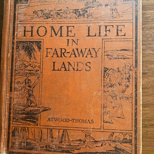 May include: An antique book titled "HOME LIFE IN FAR-AWAY LANDS" by Atwood-Thomas. The cover is orange with black illustrations of people, animals, and landscapes. The book shows signs of wear and tear.