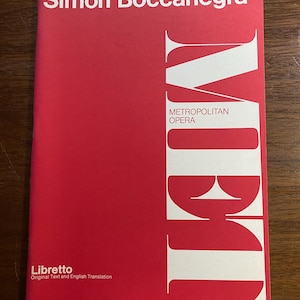 May include: A red libretto for the opera "Simon Boccanegra" by Giuseppe Verdi. The cover features white text and the words "METROPOLITAN OPERA". The text "Libretto" and "Original Text and English Translation" are also visible.