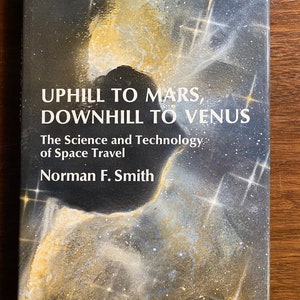 Op de afbeelding: Een boekomslag met een donkerblauwe achtergrond en een nevelachtige afbeelding in goud en wit. De titel is "Uphill to Mars, Downhill to Venus: The Science and Technology of Space Travel" door Norman F. Smith.