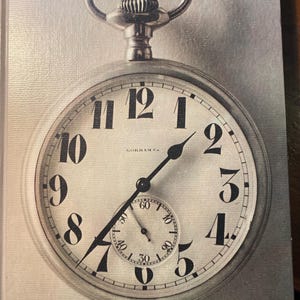 Puede incluir: Un reloj de bolsillo vintage de plata con números romanos negros en la esfera. El reloj tiene una aguja de segundos negra y un dial más pequeño para los segundos. El reloj está titulado "TIME" y forma parte de la serie "LIFE SCIENCE LIBRARY".