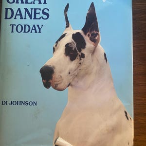 Könnte beinhalten: Ein Buch mit dem Titel "GREAT DANES TODAY" mit hellblauem Einband. Das Cover zeigt eine Nahaufnahme des Kopfes einer Deutschen Dogge, die ihre markanten schwarz-weißen Markierungen zeigt. Der Name des Autors, DI JOHNSON, ist unten aufgedruckt.