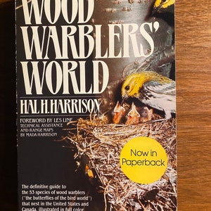 May include: Book cover with the title "Wood Warblers' World" by Hal H. Harrison. The cover features a yellow warbler with its young in a nest. The text "Now in Paperback" is on a yellow circle.