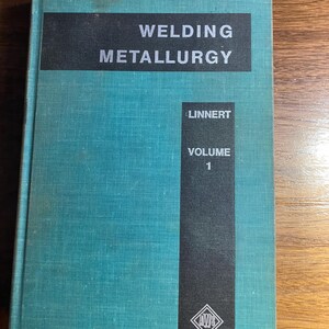 May include: A teal-colored book titled "WELDING METALLURGY" with the author's name "LINNERT" and "VOLUME 1" printed on the cover. The book has a black rectangular section at the top and a black vertical section on the right side.