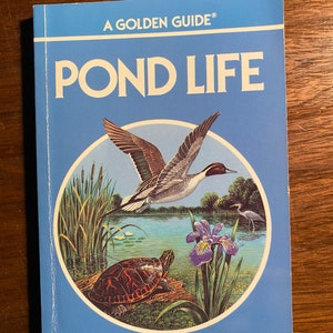 May include: A blue book with the title "A Golden Guide® Pond Life" in white text. The cover features a colorful illustration of a pond with a duck flying over the water, a turtle on a log, and a purple iris flower.