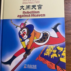 May include: A children's book titled "Rebellion against Heaven" features a cartoon monkey character in red, orange, yellow, and black. The cover includes Chinese and English text, with a blue and orange background.