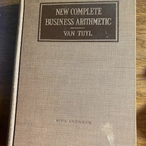 May include: A hardcover book titled New Complete Business Arithmetic by Van Tuyl with the subtitle With Answers. The book has a textured, light brown fabric cover with a dark brown rectangular border containing the title and author name.