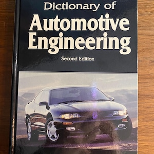 May include: A hardback book titled Dictionary of Automotive Engineering, Second Edition by Don Goodsell. The dark blue cover features white text and a photograph of a dark-coloured coupe car parked against a landscape background.