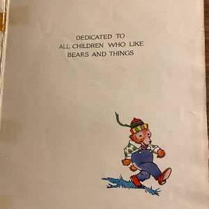 K&ouml;nnte beinhalten: Eine Widmungsseite aus einem Kinderbuch mit dem Text "Gewidmet allen Kindern, die B&auml;ren und Dinge m&ouml;gen". Die Seite zeigt eine Comic-Illustration eines B&auml;ren, der einen gr&uuml;n-gelb-roten Hut, eine blaue Latzhose und ein wei&szlig;es Hemd mit gr&uuml;nen Punkten tr&auml;gt. Der B&auml;r geht auf einem blau-gr&uuml;nen Weg.