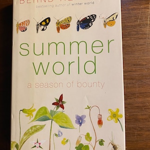 May include: Book cover with the title "Summer World: A Season of Bounty" by Bernd Heinrich, bestselling author of "Winter World". The cover features colorful illustrations of butterflies and wildflowers.