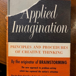 Può includere: Un libro vintage intitolato "Applied Imagination: Principles and Procedures of Creative Thinking" di Alex F. Osborn, Ph.M. La copertina del libro è arancione e nera con il titolo in testo bianco. Il libro è un'edizione rivista e si descrive come "Dall'ideatore del Brainstorming".