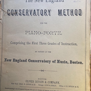 Op de afbeelding: Oude boekcover met de titel "The New England Conservatory Method" voor piano-forte. De cover, met zwarte tekst, toont slijtage en de details van de uitgever. Voor de eerste drie lesniveaus.