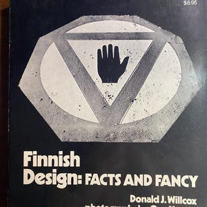 May include: A book cover with the title "Finnish Design: FACTS AND FANCY" in white text on a black background. The cover features a geometric design with a hand symbol. The author is Donald J. Willcox, with photographs by Ove Hector.