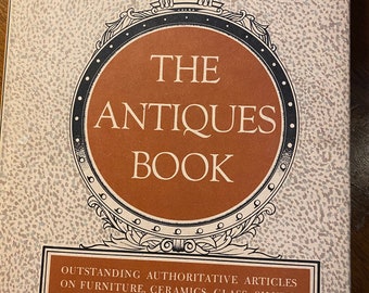 May include: The cover of a book titled "The Antiques Book" with an illustration of an eagle perched on a circular frame. The book features articles on furniture, ceramics, glass, silver, pewter, and other collecting interests. It is illustrated with photographs of over two hundred items and edited by Alice Winchester and the staff of The Magazine Antiques.