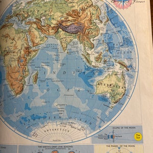 May include: A vintage world map with a blue background and green and brown landmasses. The map shows the continents of the world, including North America, South America, Europe, Asia, Africa, Australia, and Antarctica. The map also shows the oceans, including the Pacific Ocean, Atlantic Ocean, Indian Ocean, and Arctic Ocean. The map is surrounded by a white border and includes a compass rose and a key to the map's symbols.