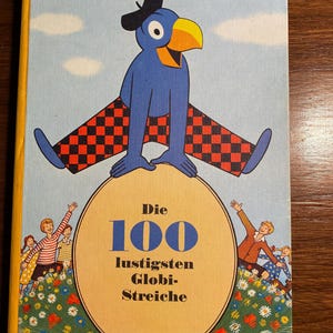 May include: A vintage children's book titled "Die 100 lustigsten Globi-Streiche." The cover features a blue bird character with a black hat and checkered pants, perched on a yellow circle. The background is light blue with white clouds and illustrations of children.