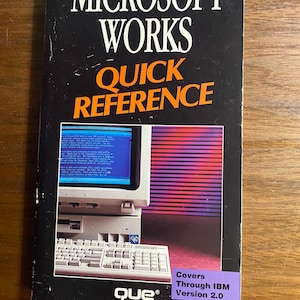 May include: A Microsoft Works Quick Reference book with a black cover. The title is in white and orange text. The cover features an image of a computer monitor and keyboard. The book is labeled "Covers Through IBM Version 2.0" and the publisher is "que".