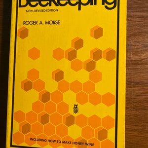Puede incluir: Una cubierta de libro amarilla con el título "The Complete Beekeeping" en texto negro. El libro es una nueva edición revisada por Roger A. Morse. La cubierta presenta un patrón de panal con una abeja en el centro y el texto "Including How to Make Honey Wine".