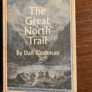 May include: The cover of a book titled "The Great North Trail" by Dan Cushman. The book is part of "The American Trails Series" edited by A.B. Guthrie Jr. The cover features a vintage illustration of a group of people travelling through a forest.