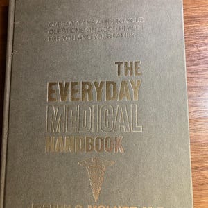 Pode incluir: Um livro de capa dura intitulado "The Everyday Medical Handbook" com letras douradas e um símbolo médico. A capa é de cor dourada suave e o nome do autor, Joseph G. Molner, M.D., está na parte inferior.