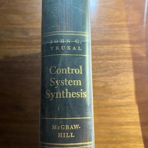 May include: A dark blue hardcover book spine with gold lettering. The text reads John G. Truxal, Control System Synthesis, and McGraw-Hill. There are thin gold horizontal lines above and below the author name and publisher name, with vertical red lines.