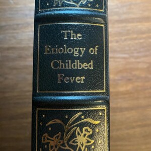 以下が含まれることがあります： 背表紙に金色の文字が書かれた緑色の革装丁の本。タイトルは「The Etiology of Childbed Fever」です。