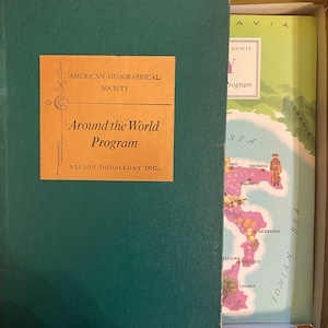 Pode incluir: Uma caixa verde com um rótulo dourado que diz "American Geographical Society Around the World Program Nelson Doubleday Inc." A caixa está aberta e um mapa da Itália é visível no interior.