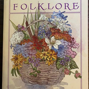 Może przedstawiać: Książka w twardej oprawie zatytułowana Wildflower Folklore autorstwa Laury C. Martin. Okładka przedstawia akwarelową ilustrację plecionego kosza wypełnionego różnorodnymi kolorowymi polnymi kwiatami, w tym żółtymi stokrotkami i niebieskimi kwiatami.