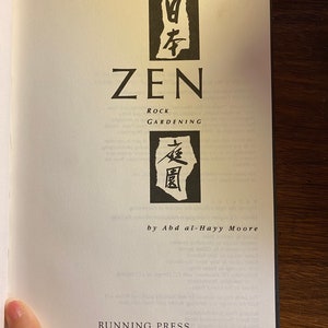 Pode incluir: Capa de livro com o título "Zen Rock Gardening" em texto preto. O livro é de Abd al-Hayy Moore e é publicado pela Running Press.