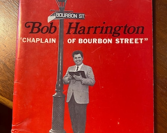 May include: A red book cover with the title "crusade songs" and a photo of a man in a suit standing in front of a street lamp. The text "Bob Harrington 'CHAPLAIN OF BOURBON STREET'" is printed below the title. The book cover also includes the text "...Go ye into the world and preach the gospel to all creatures," Mark 16:15.
