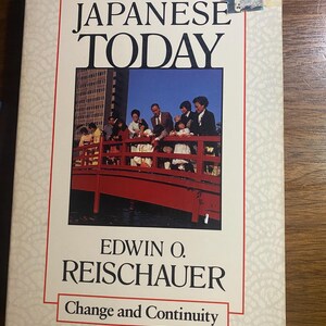 Op de afbeelding: Een boek getiteld "The Japanese Today" van Edwin O. Reischauer. De omslag toont een foto van mensen op een rode brug met een gebouw op de achtergrond. De ondertitel luidt "Change and Continuity".