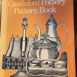 May include: The Castleford Pottery Pattern Book cover features a black and white illustration of a teapot, sugar bowl, and other serving pieces on a wooden tray. The book cover is orange.