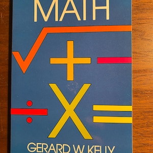 May include: A blue book cover with the title "SHORT-CUT MATH" in white letters. The cover features a yellow multiplication symbol, a red division symbol, a red minus sign, a yellow plus sign, and an orange square root symbol. The author's name, "GERARD W. KELLY", is printed in white letters at the bottom of the cover.