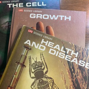 May include: A stack of vintage Life Science Library books. The titles visible are "The Cell", "Growth", and "Health and Disease". The cover of "Health and Disease" features a syringe and a detailed illustration of a fly.