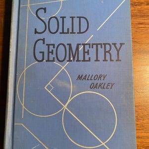 Puede incluir: Un libro de tapa dura azul titulado "Solid Geometry" de Mallory Oakley. La portada presenta un diseño geométrico de círculos y líneas.