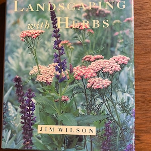 Puede incluir: Portada de libro con una foto de flores rosas y moradas con hojas verdes. El título es "Landscaping with Herbs" de Jim Wilson.