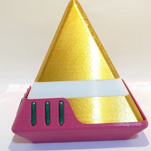 May include: A pink and gold pyramid-shaped box with a white stripe and green accents. The box is closed.