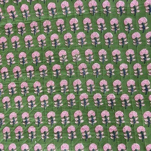 May include: Green fabric with a repeating pattern of pink floral designs. The flowers have a detailed, textured appearance, and the fabric has a quilted effect. The overall design is symmetrical and visually appealing.