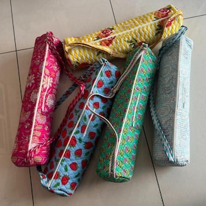 May include: A collection of colorful yoga mat bags. The bags feature various patterns, including floral, strawberry, and geometric designs. Each bag has a zipper closure and a rope handle. The bags are in shades of pink, blue, green, and yellow.