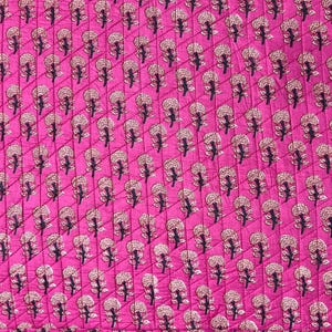May include: A quilted fabric with a vibrant pink background. The pattern features a repeating design of stylized floral elements in cream and black. The fabric has a textured appearance due to the quilting.