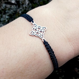 May include: A black braided bracelet with a silver Celtic knot charm.