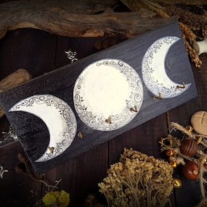 Puede incluir: Un colgador de llaves de madera con tres formas de luna creciente pintadas en blanco y gris con intrincados diseños florales. Cada luna tiene un gancho de latón para colgar las llaves.