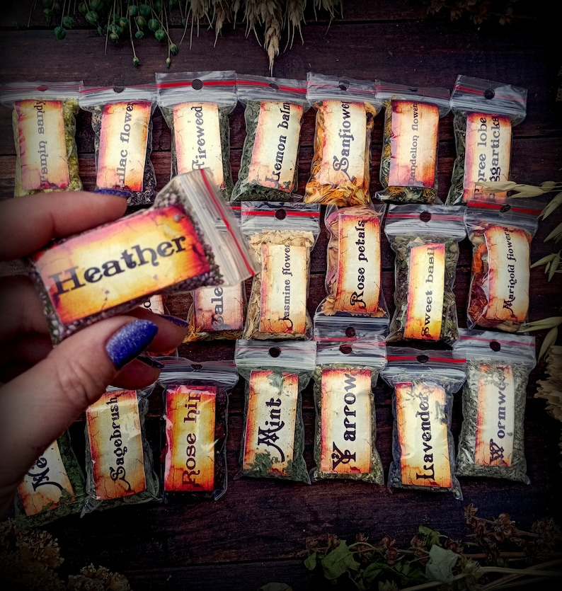 May include: A collection of small, clear plastic bags filled with dried herbs and flowers. Each bag has a label with the name of the herb or flower written on it. The labels are in a vintage style with a brown background and white lettering. The herbs and flowers include: Heather, Sagebrush, Rose hip, Mint, Lemon balm, Jasmine flower, Sanfiowe, arrow, Rose petals, Dandelion flower, Isavender, Sweet basil, Wormwood, Phree lobe, 3garticks, Marigold flower.