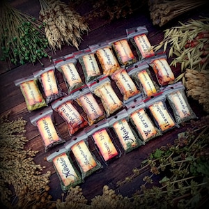 May include: A collection of small, clear plastic bags filled with dried herbs and flowers. The bags are labeled with the names of the herbs and flowers, such as "Lemon Balm", "Fireweed", "Heather", and "Rose Petals".