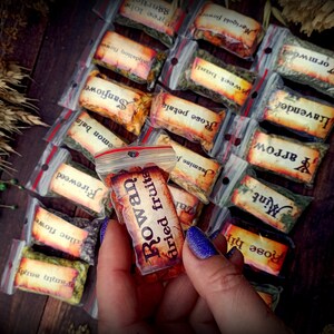 May include: A variety of small, clear plastic bags filled with dried herbs and flowers. Each bag has a label with the name of the herb or flower written in a rustic font. The bag in the center of the image is labeled "Rowan dried fruits".