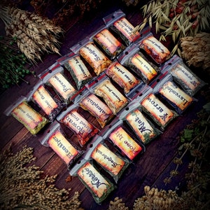 May include: A collection of small, clear plastic bags filled with dried herbs and flowers. Each bag has a handwritten label with the name of the herb or flower, such as "Sagebrush", "Rose hip", "Mint", and "Lavender".